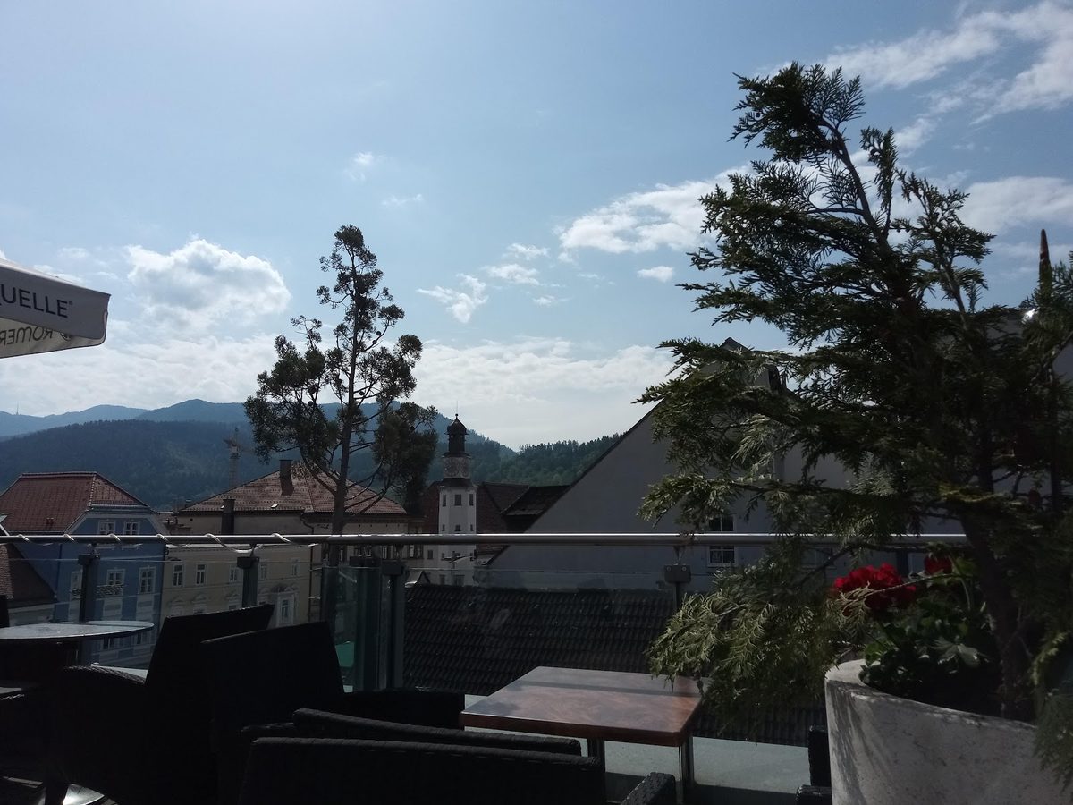 Holztische und Sessel auf der Sonnenterrasse mit Blick auf die Hügel um Leoben