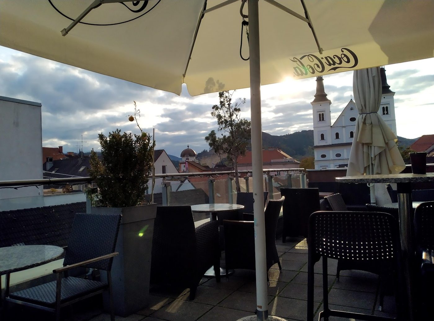 Die Terrasse des Café Bellini mit Sonnenschirm und Bestuhlung, dahinter der Blick über die Dächer von Leoben